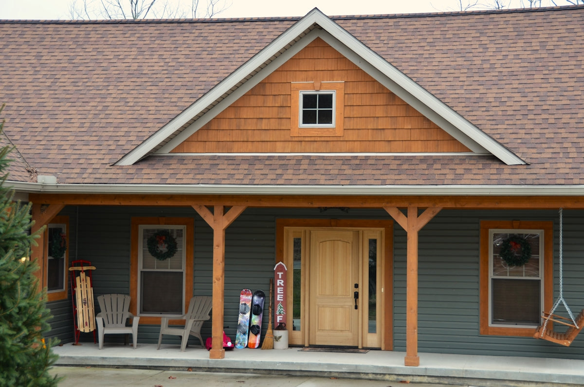 a gray house with a brown roof and two chairs on the front porch